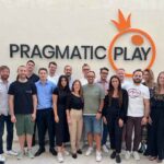 tim Pragmatic Play di kantor dengan logo perusahaan di belakang